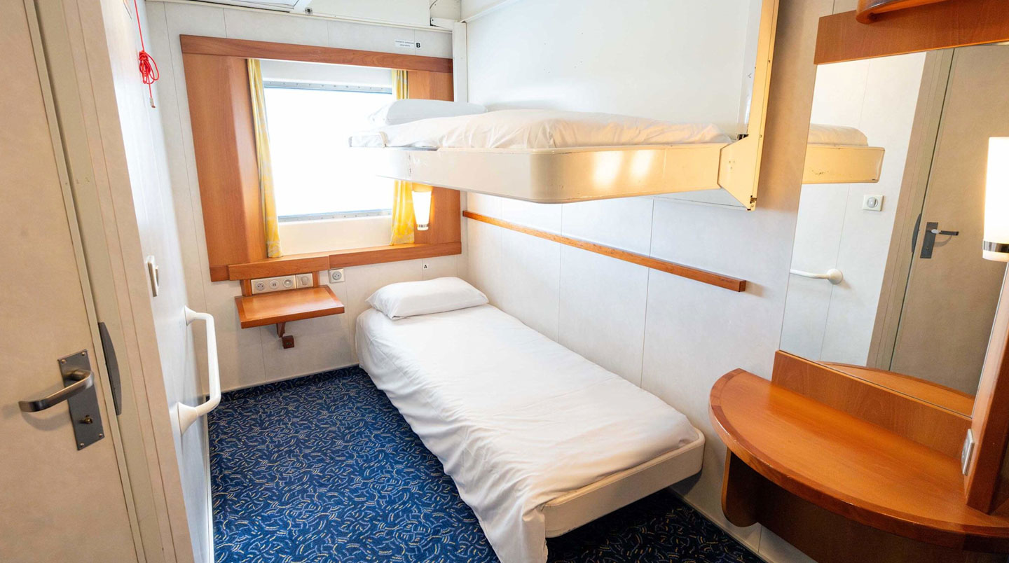Familie in sommerlicher Freizeitkleidung steht an der Reling eines Fährdecks und blickt aufs Meer, von hinten fotografiert, moderne Fährstruktur sichtbar