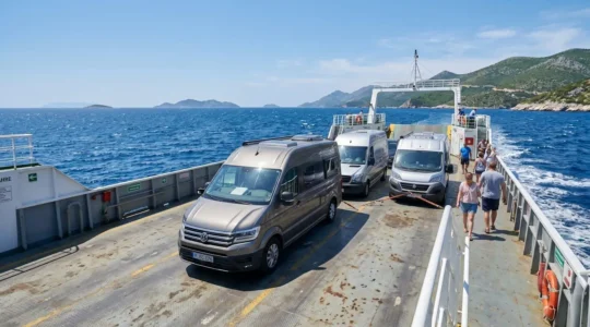 Ein Wohnmobil steht auf dem offenen Autodeck einer modernen Fähre, im Hintergrund leuchtet das tiefblaue Mittelmeer unter klarem Himmel
